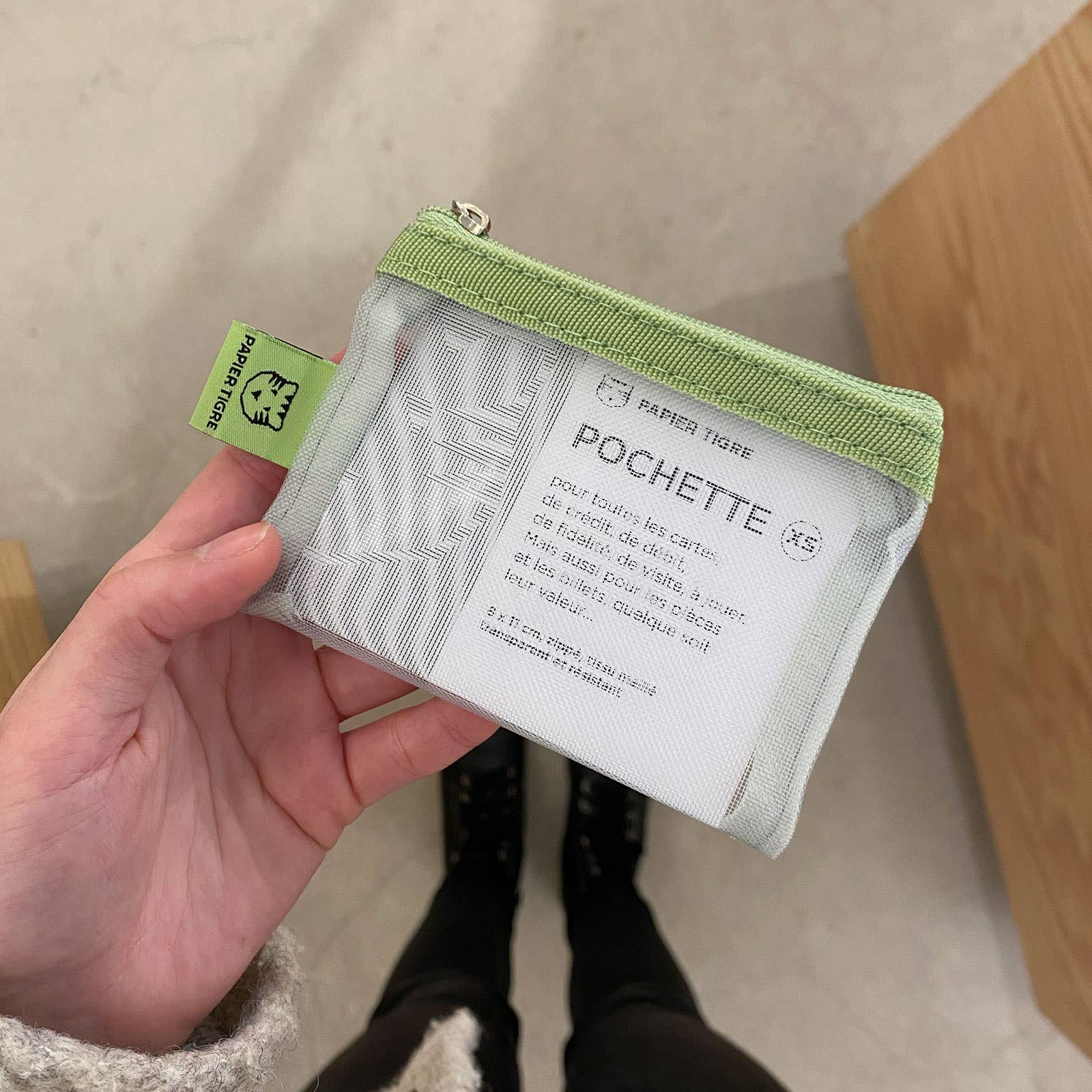 Small pouch with green trim held by a hand, against a neutral background