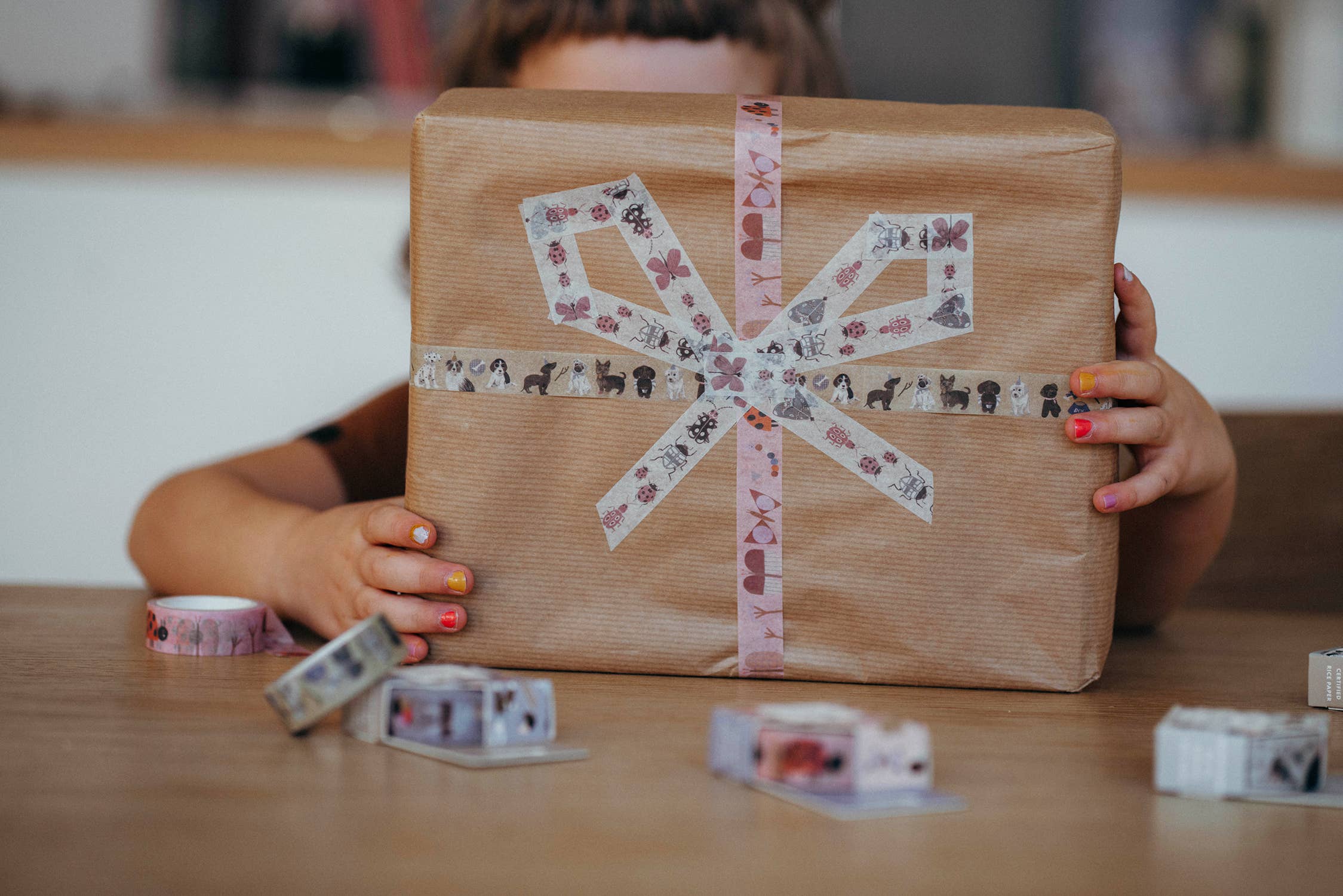 Person holding a wrapped gift with decorative tape in a kitchen setting