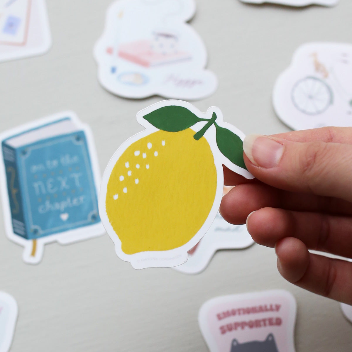 Hand holding a lemon-shaped sticker with other decorative stickers in the background.