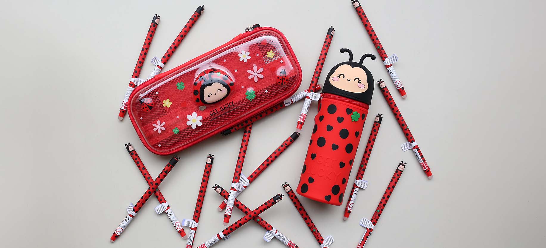 Two red pencil cases with ladybug design surrounded by red ladybug pens on a light grey background