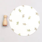 Round white plate with gold leaf pattern next to a wooden stamp on a light gray background