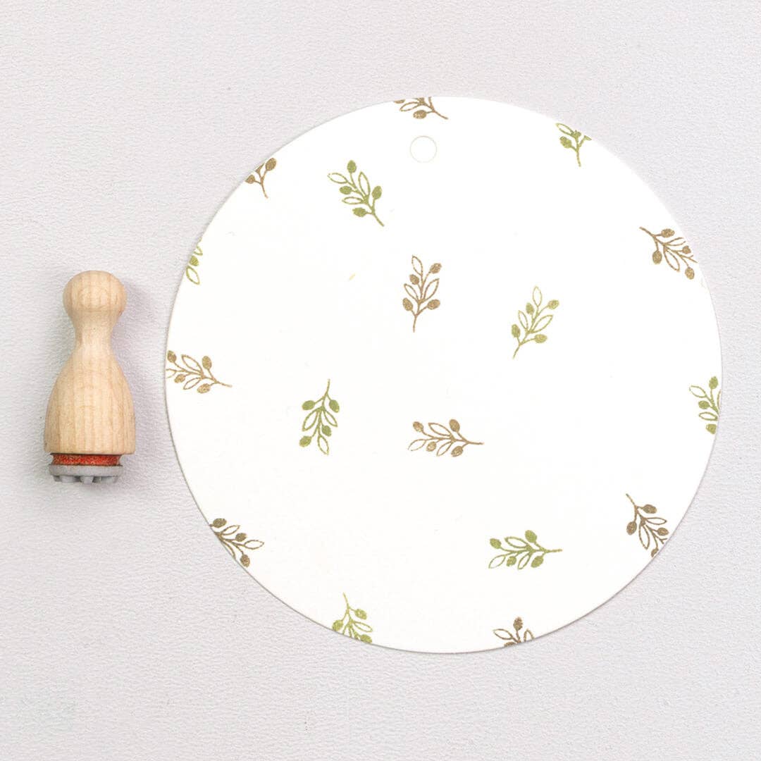 Round white plate with gold leaf pattern next to a wooden stamp on a light gray background