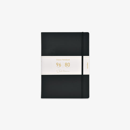 A black hardcover notebook with an elastic closure band and a white paper band around the middle, featuring gold text that reads 'Classic Notebook 96 sheets and 80gsm'.