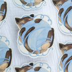 Vinyl sticker of a cat wrapped in blue yarn on a light blue background