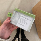 Small pouch with green trim held by a hand, against a neutral background