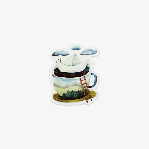 A die-cut sticker featuring a whimsical illustration of a sailboat floating on a cup of coffee with mountains and clouds, shown on a plain light gray background.