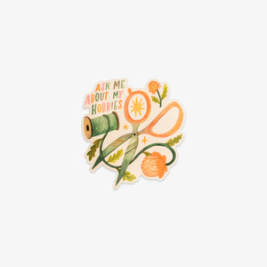 Sticker with scissors, thread, and flowers with text 'Ask me about my hobbies' on a white background