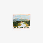 A rectangular sticker with rounded corners featuring a hand-drawn landscape illustration of mountains, a winding river, and green fields. The sticker has an orange border and the text 'ENJOY THE VIEW' printed at the bottom.