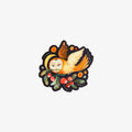 A die-cut sticker featuring a whimsical illustration of an owl with closed eyes, orange wings, and a yellow hat, nestled among green leaves and red berries on a black background.