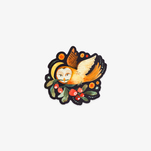 A die-cut sticker featuring a whimsical illustration of an owl with closed eyes, orange wings, and a yellow hat, nestled among green leaves and red berries on a black background.