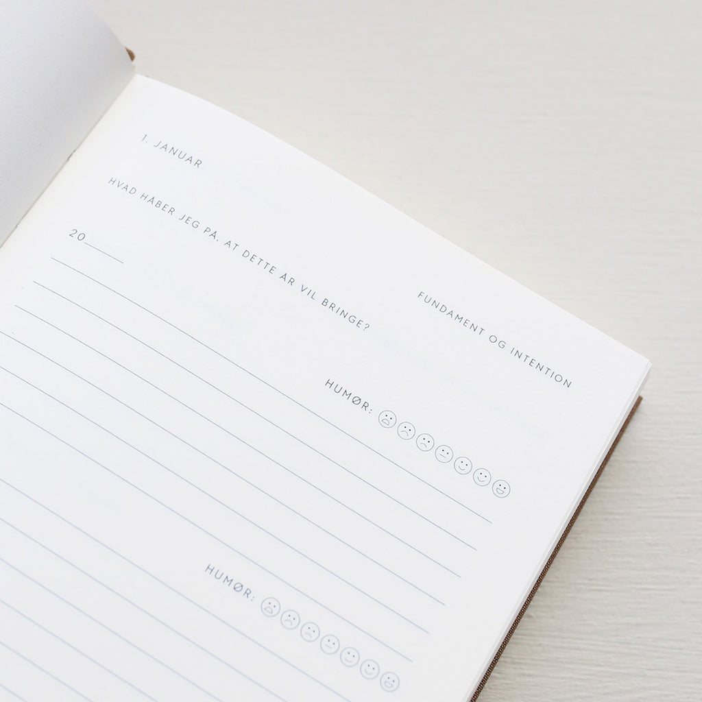Open notebook with a page showing text and emoji icons from 'Treårsdagbogen' on a light background