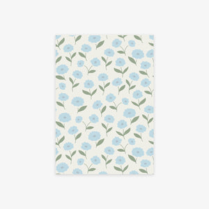 A rectangular sheet of paper with a repeating floral pattern of light blue flowers and green leaves on an off-white background, shown against a light gray studio backdrop.