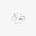 Vinyl sticker of a green and brown bicycle with a cute little dog in a basket, labeled 'Danmark' on a light pink background