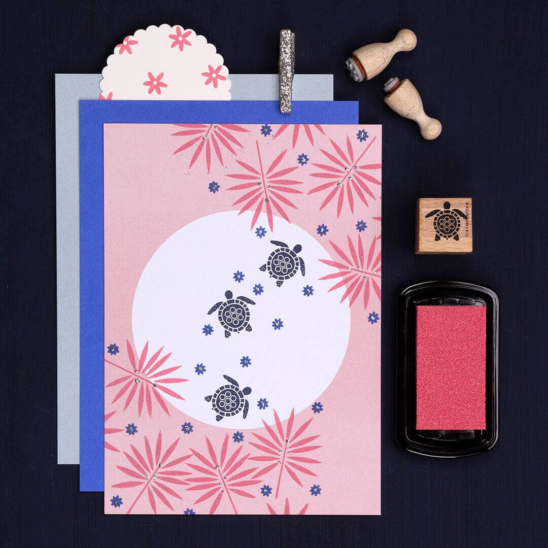 Card with turtle design and floral patterns, surrounded by stamps and ink pad on a dark background