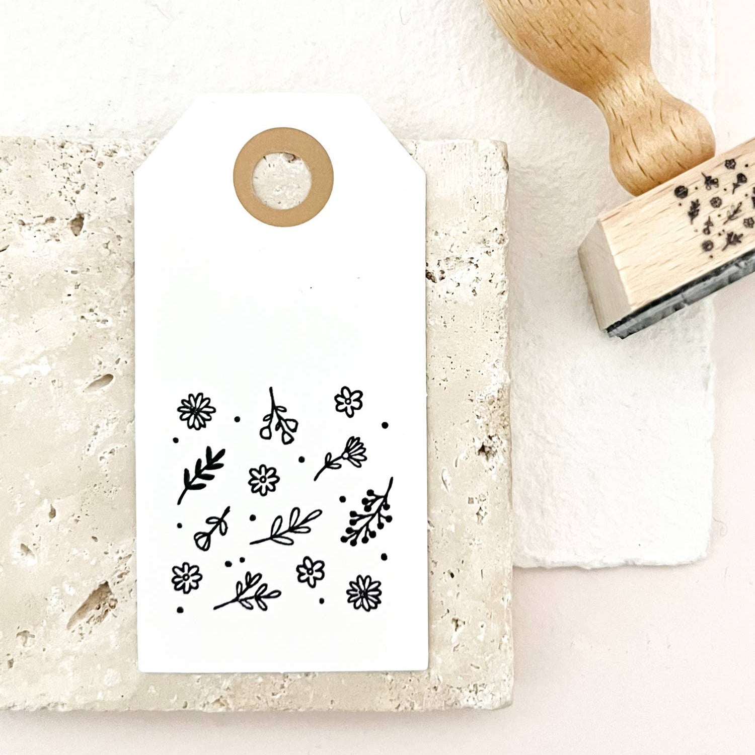Decorative stamp with floral design on a white card, next to a wooden handle stamp on a light background.