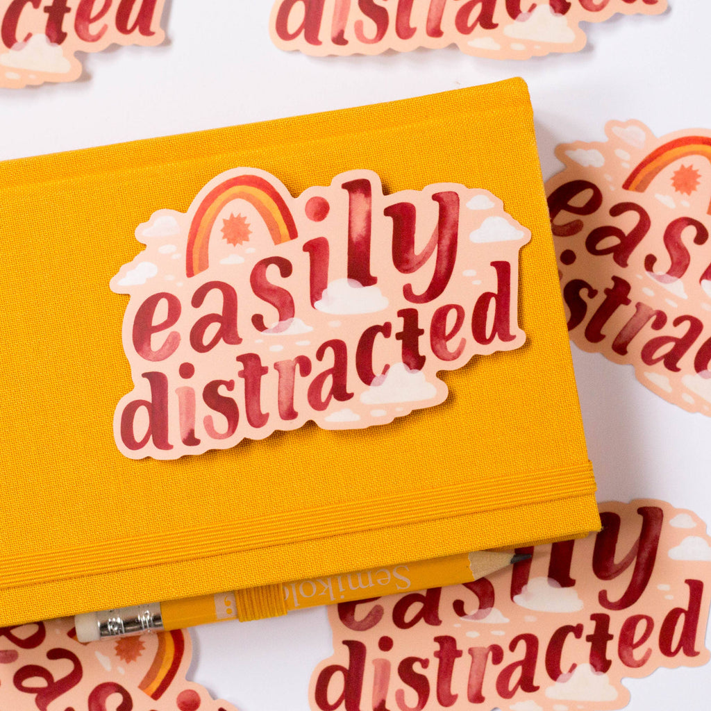 Yellow notebook with 'easily distracted' sticker on a white background with scattered text.