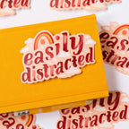 Yellow notebook with 'easily distracted' sticker on a white background with scattered text.
