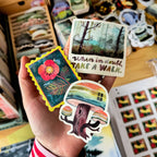 Hand holding colorful stickers with nature-themed designs and text.